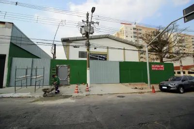 Vista externa frontal de galpão, em fase final de reforma, com muro verde, 2 portões de acesso de caminhões e porta para pedestres..